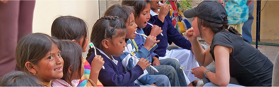 a volunteer is teaching children how to brush teeth